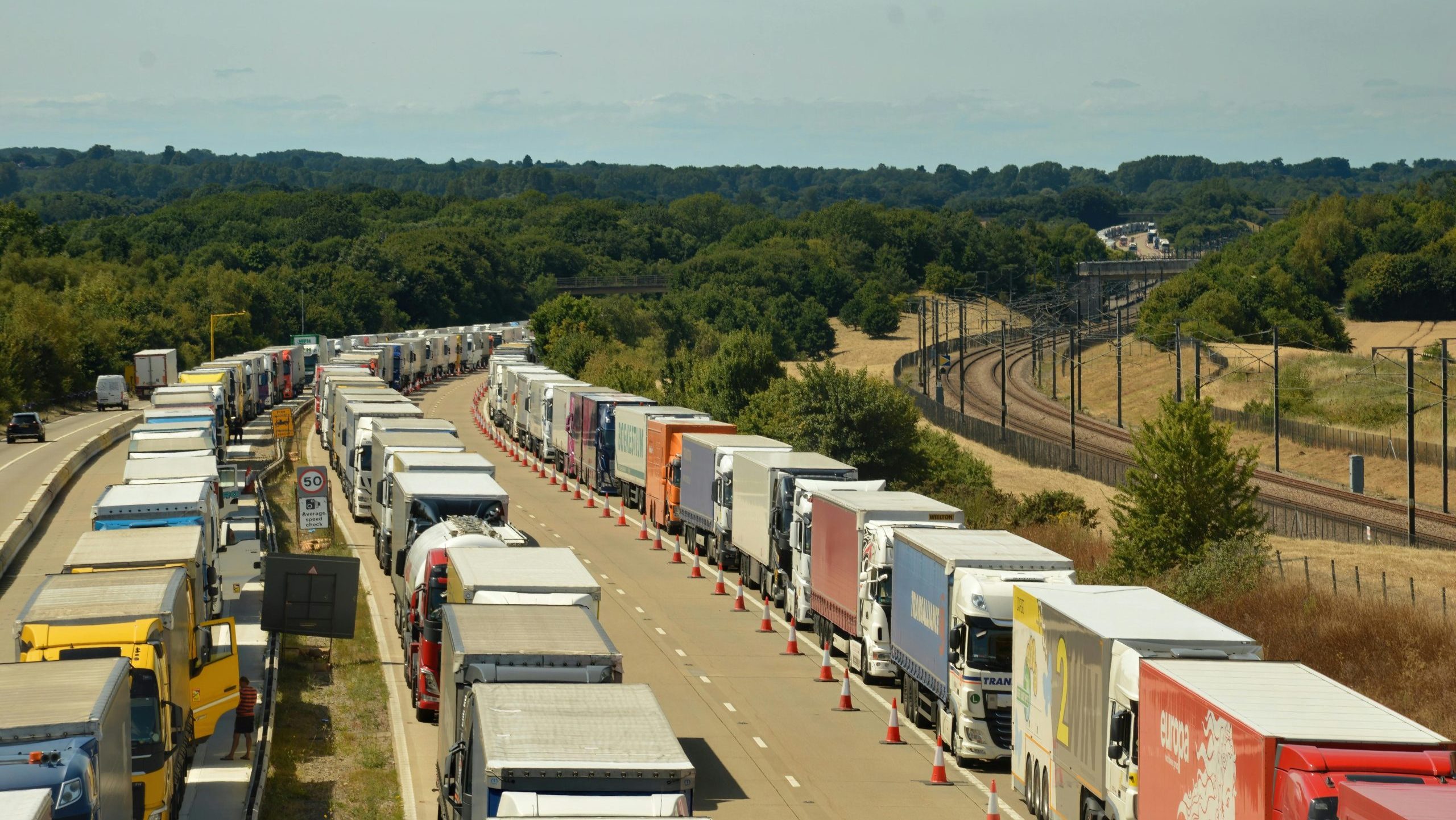 Long queue of trucks on an English highway amidst scenic countryside.